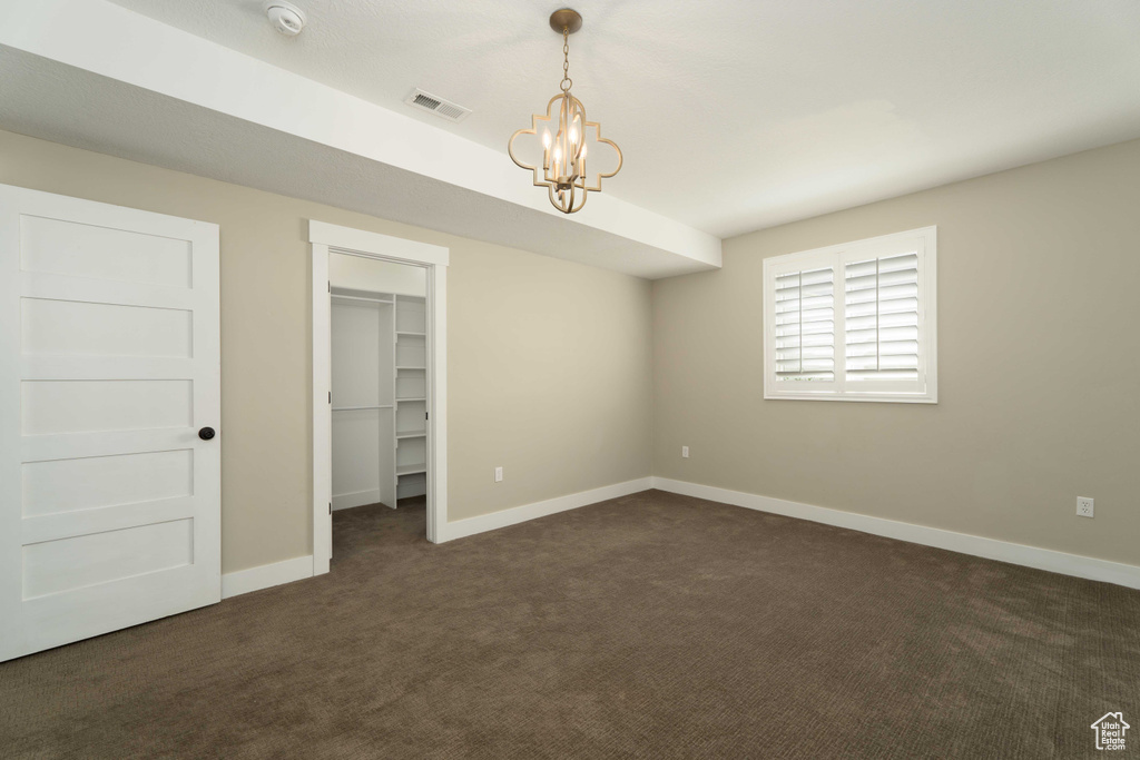 Unfurnished bedroom featuring an inviting chandelier, dark carpet, a walk in closet, and a closet