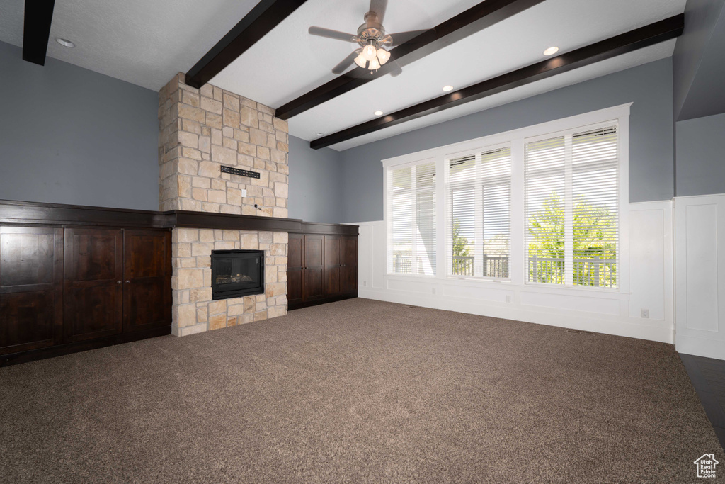 Unfurnished living room featuring a stone fireplace, beamed ceiling, carpet, and ceiling fan