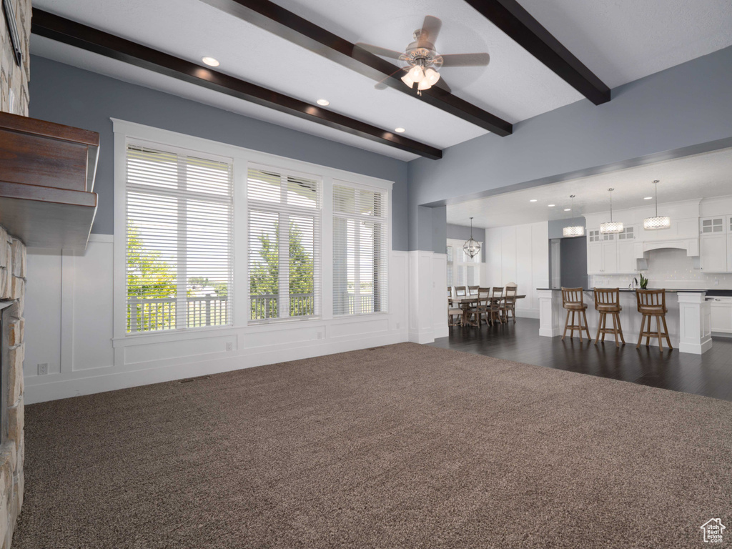 Unfurnished living room featuring a stone fireplace, dark wood-type flooring, ceiling fan, and beam ceiling