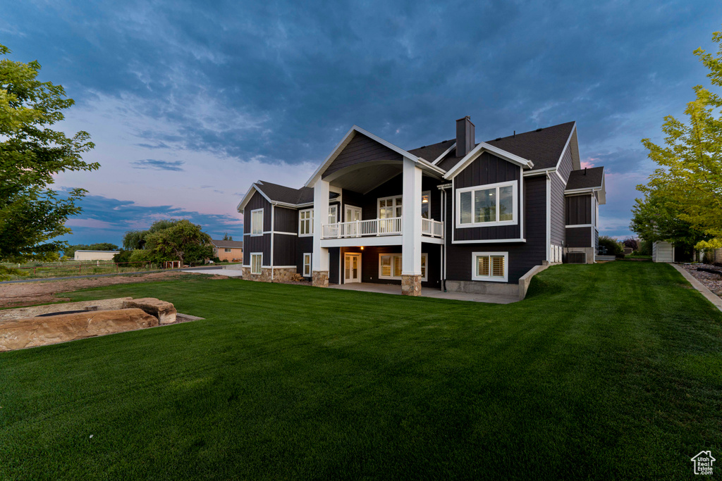 Back house at dusk with a balcony and a lawn