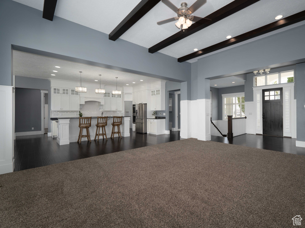 Living room with a high ceiling, dark wood-type flooring, ceiling fan, and beam ceiling