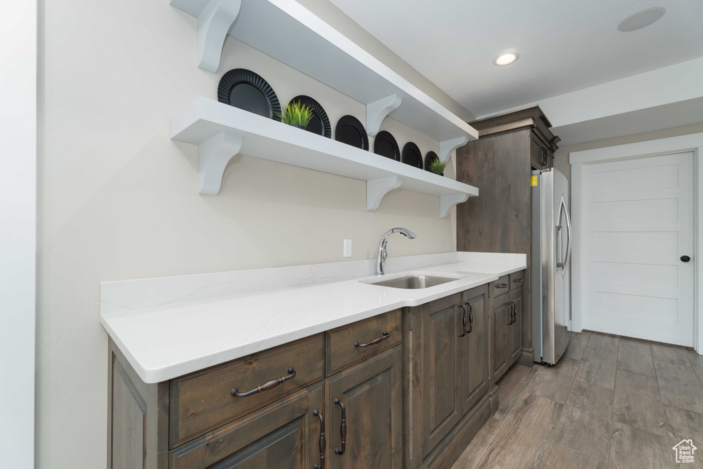 Kitchen featuring dark brown cabinets, sink, light stone counters, light hardwood / wood-style flooring, and stainless steel refrigerator