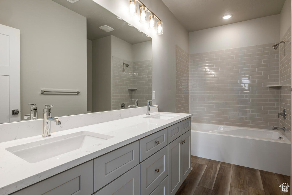 Bathroom with wood-type flooring, double sink vanity, and tiled shower / bath combo