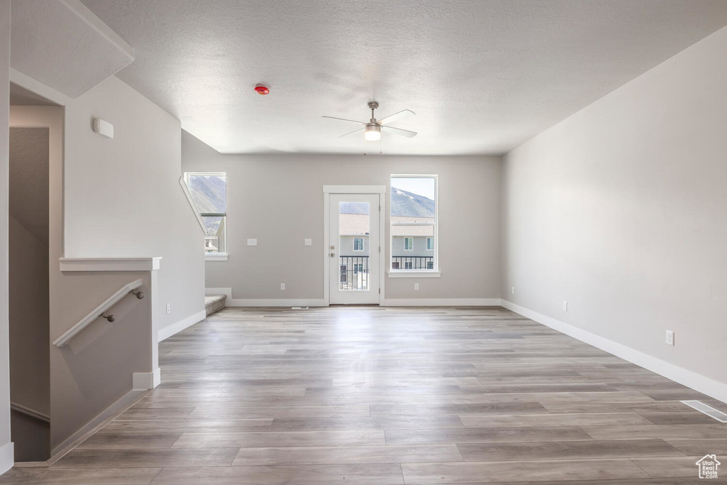 Unfurnished living room with ceiling fan, a textured ceiling, and hardwood / wood-style flooring