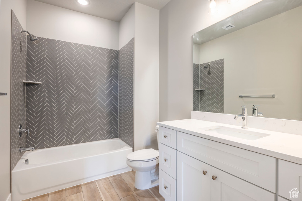 Full bathroom with wood-type flooring, toilet, tiled shower / bath combo, and vanity