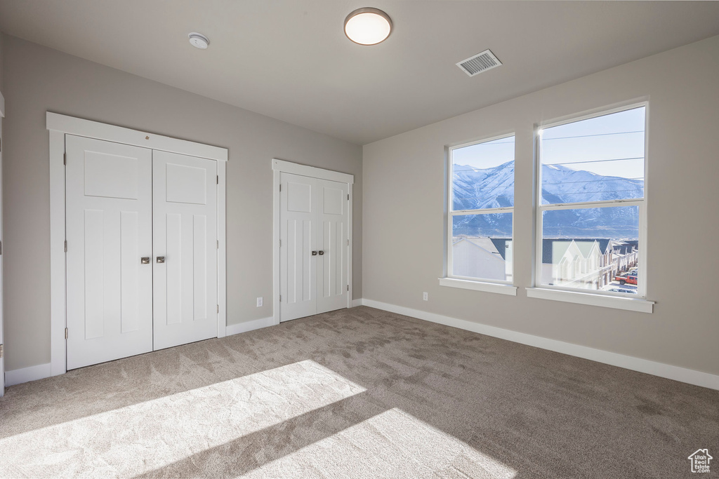 Unfurnished bedroom featuring two closets, multiple windows, and light carpet