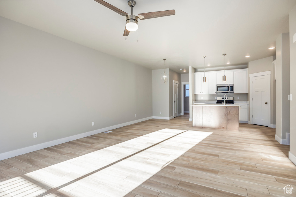 Kitchen featuring white cabinets, light hardwood / wood-style floors, ceiling fan, and an island with sink