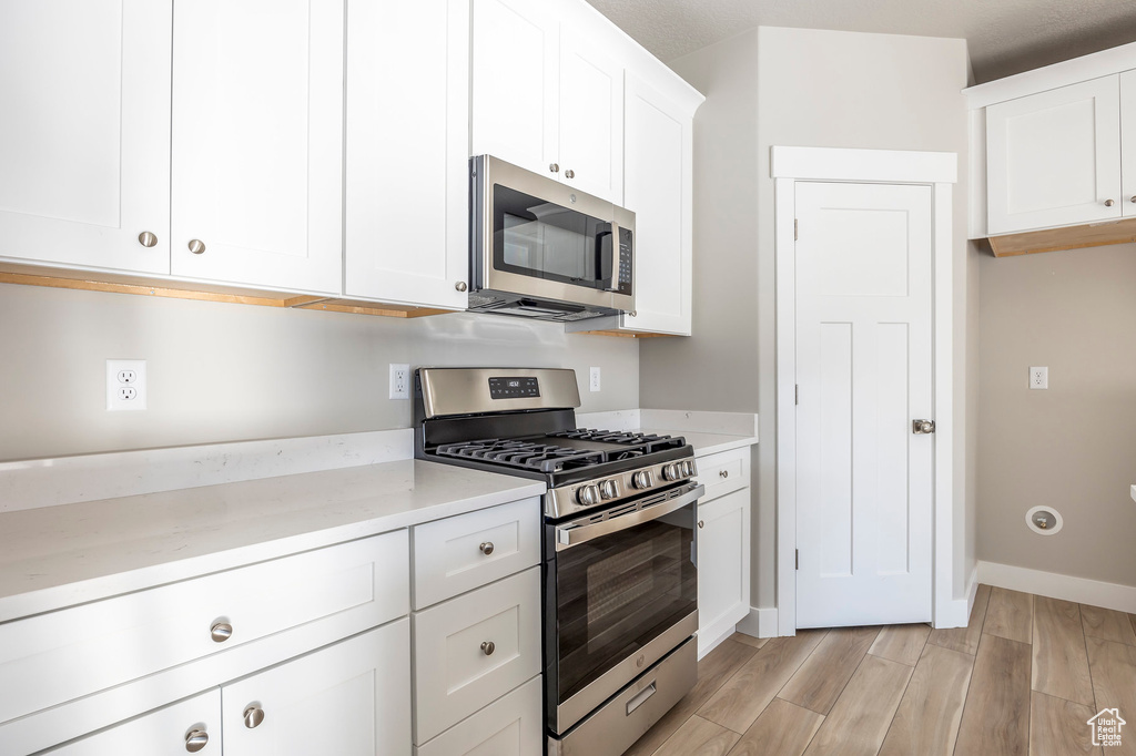 Kitchen featuring appliances with stainless steel finishes, light stone counters, white cabinets, and light wood-type flooring