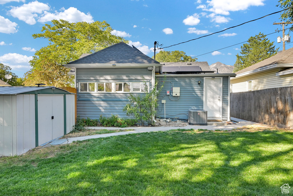 Rear view of property featuring central AC unit, a shed, and a yard