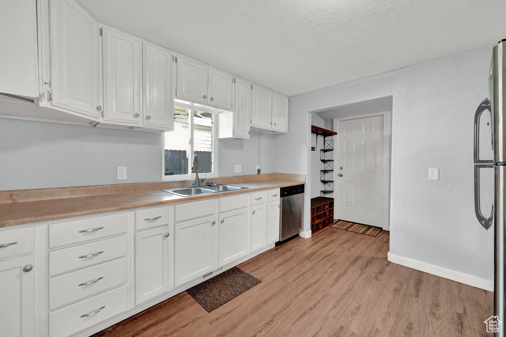 Kitchen with sink, a textured ceiling, white cabinetry, appliances with stainless steel finishes, and light wood-type flooring