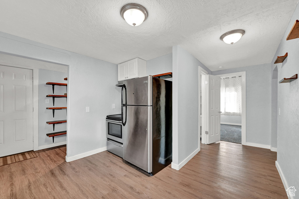 Kitchen with light hardwood / wood-style flooring, a textured ceiling, appliances with stainless steel finishes, and white cabinetry