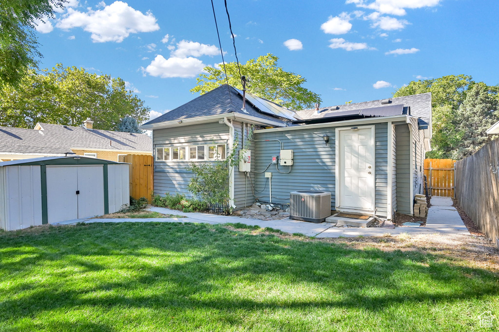 Rear view of property featuring a shed, cooling unit, and a lawn