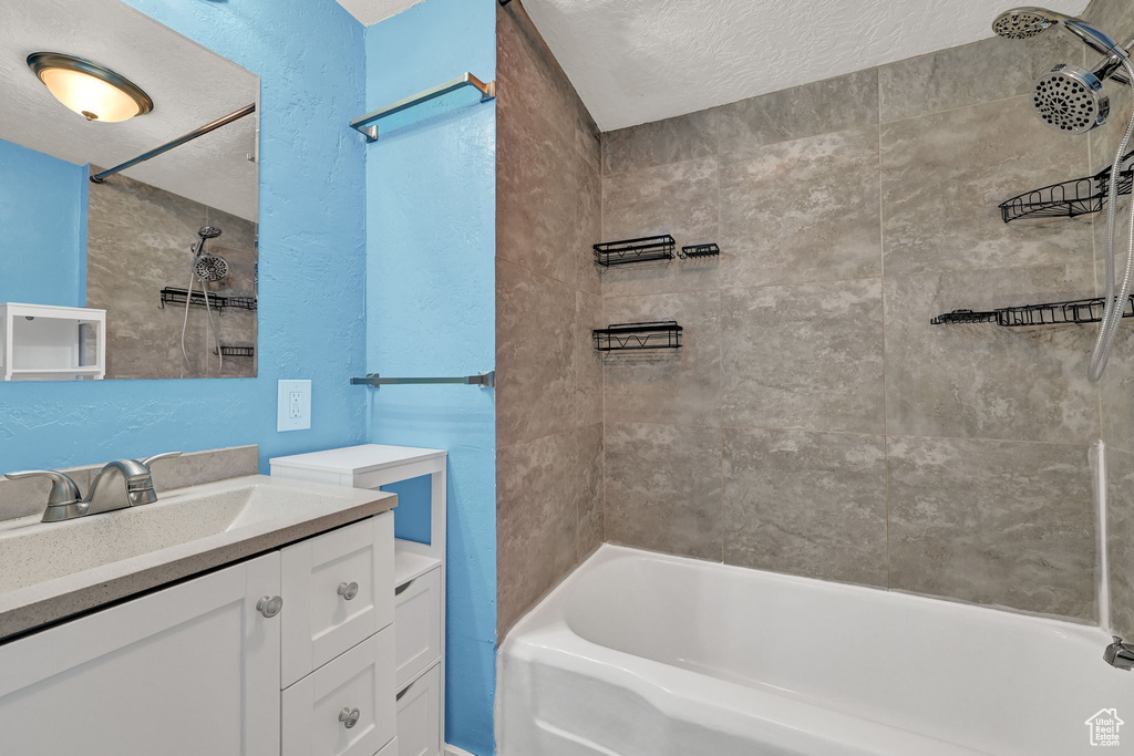 Bathroom featuring a textured ceiling, tiled shower / bath, and vanity