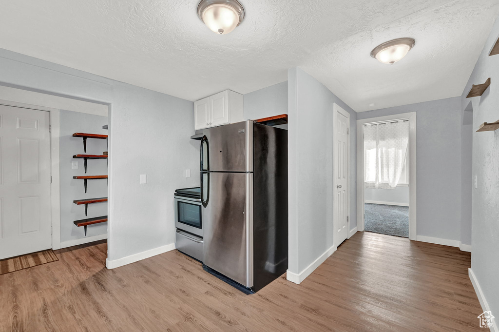 Kitchen featuring white cabinets, a textured ceiling, stainless steel appliances, and light wood-type flooring