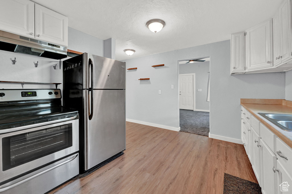 Kitchen with white cabinets, a textured ceiling, appliances with stainless steel finishes, range hood, and light hardwood / wood-style floors