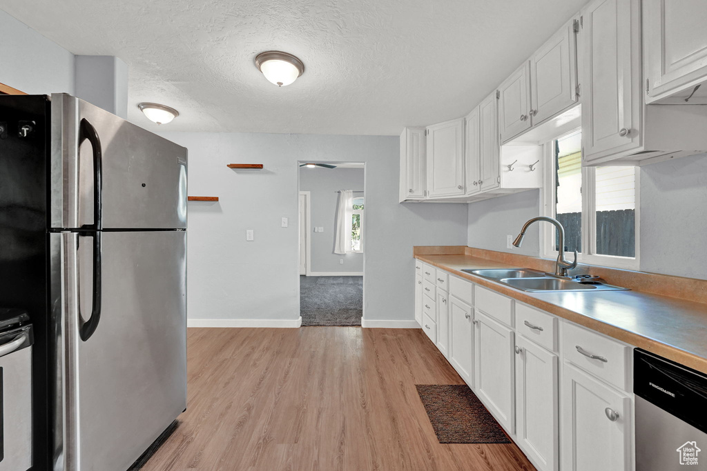 Kitchen with white cabinets, sink, a textured ceiling, light hardwood / wood-style flooring, and appliances with stainless steel finishes