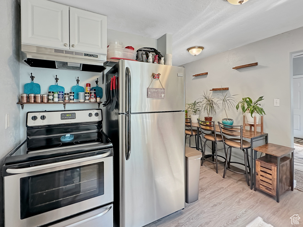 Kitchen with appliances with stainless steel finishes, light wood-type flooring, and white cabinets