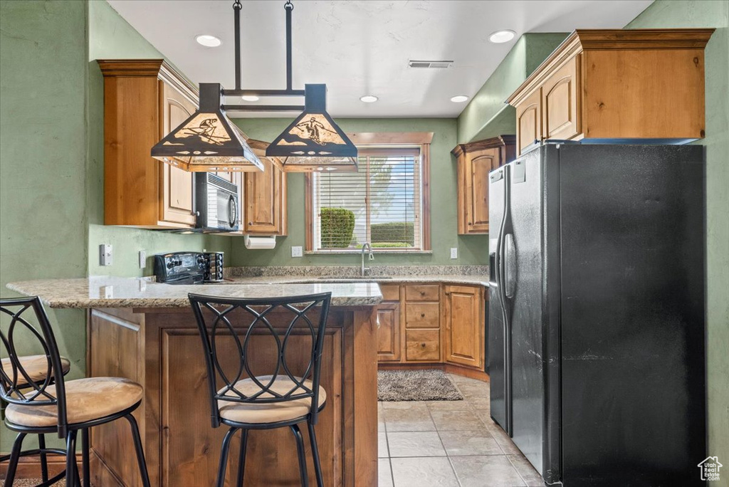 Kitchen with light tile patterned floors, black appliances, sink, a kitchen bar, and kitchen peninsula