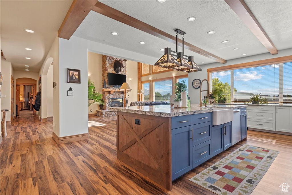 Kitchen featuring a textured ceiling, a stone fireplace, hanging light fixtures, wood-type flooring, and beam ceiling