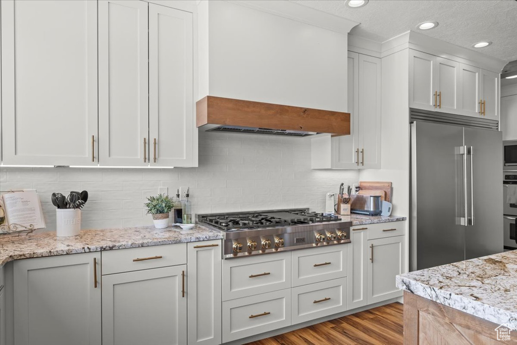 Kitchen featuring backsplash, white cabinetry, light hardwood / wood-style floors, and built in appliances