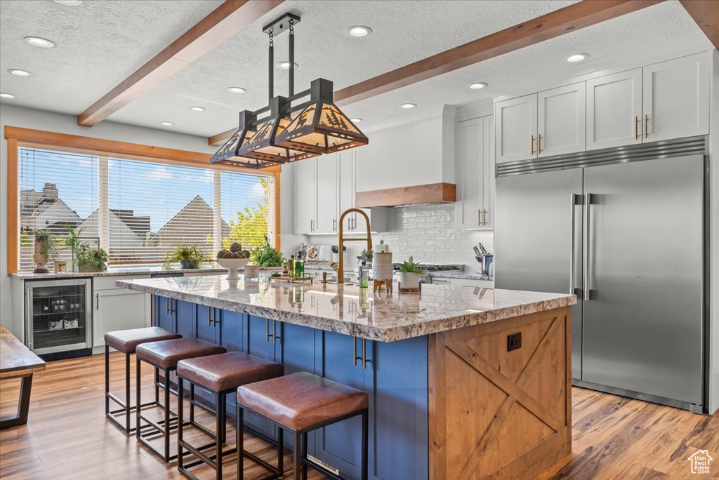 Kitchen featuring white cabinets, wine cooler, built in fridge, beam ceiling, and decorative light fixtures