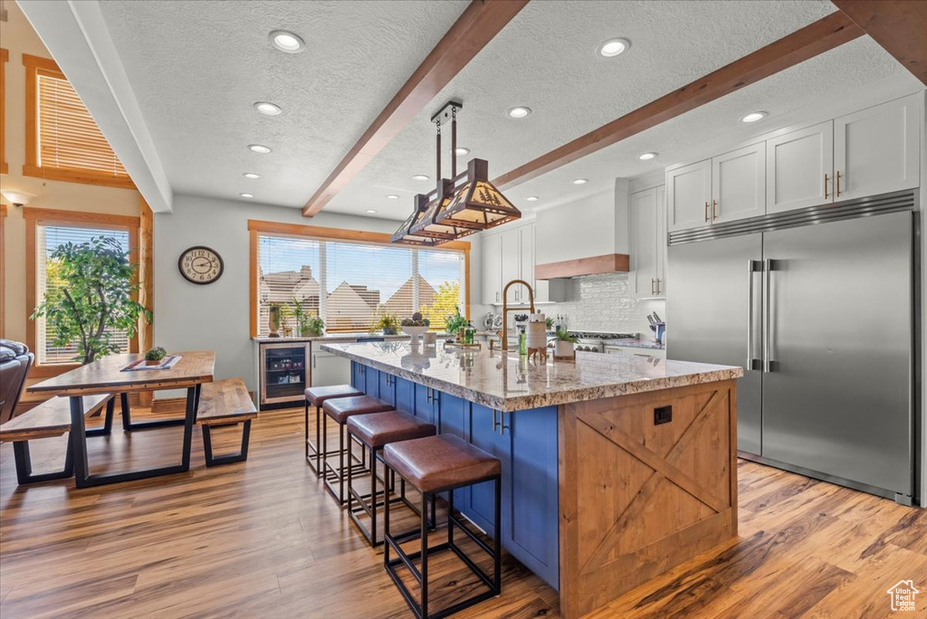 Kitchen featuring white cabinetry, pendant lighting, built in refrigerator, beamed ceiling, and an island with sink