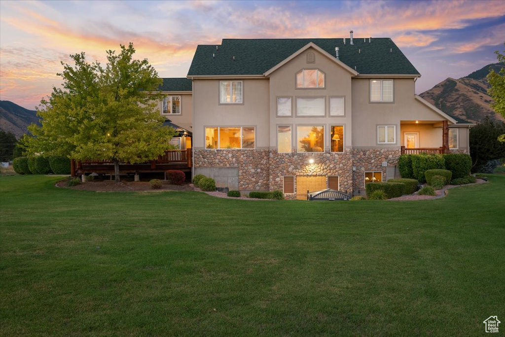 Back house at dusk featuring a yard and a deck