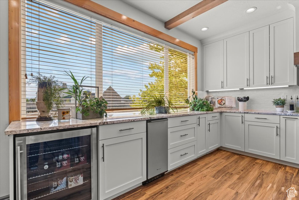 Interior space with wine cooler, light hardwood / wood-style floors, backsplash, beam ceiling, and white cabinetry