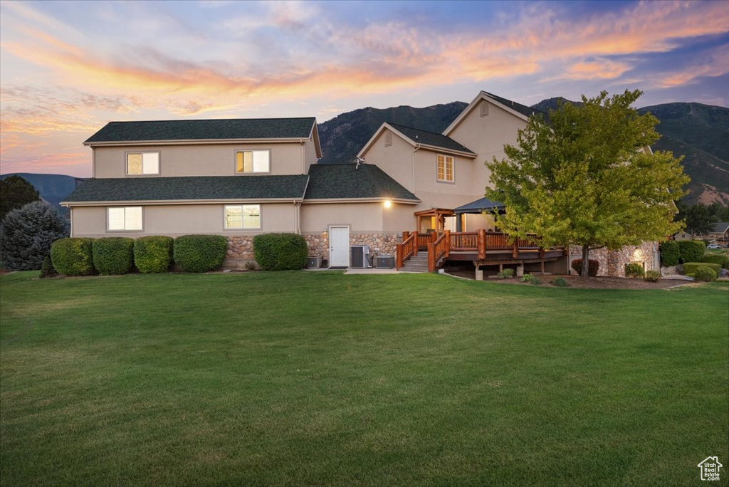 Back house at dusk featuring a deck with mountain view and a lawn