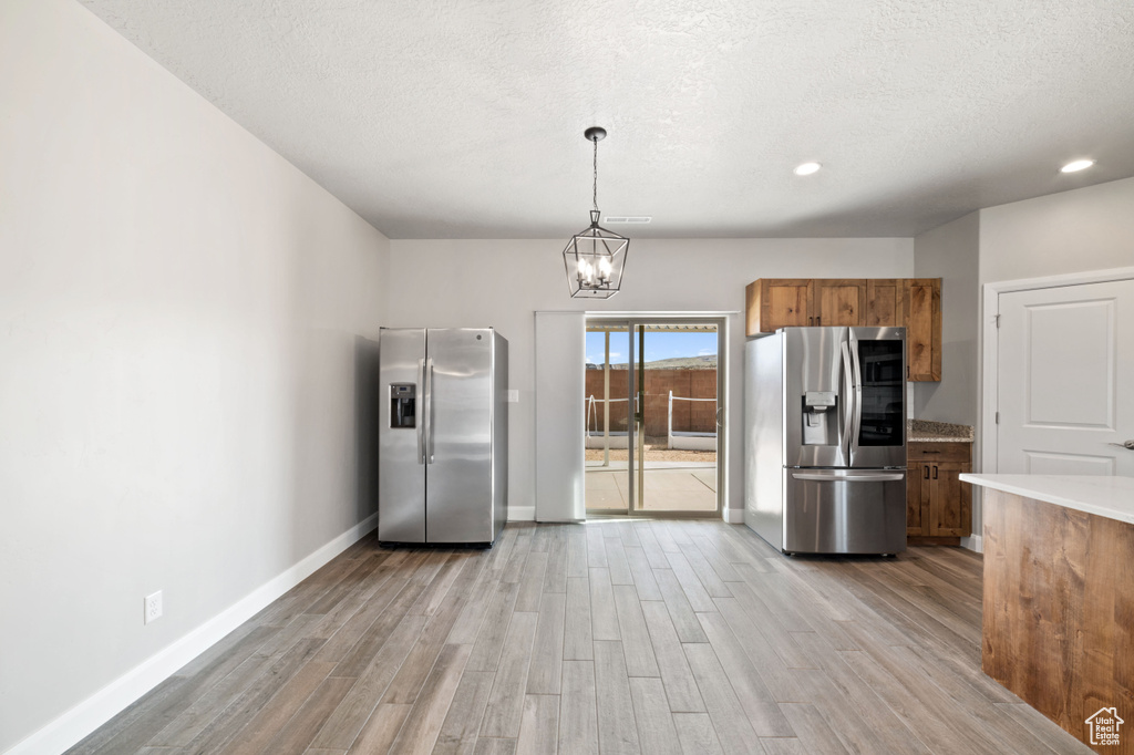 Kitchen with stainless steel fridge, decorative light fixtures, light hardwood / wood-style floors, and an inviting chandelier