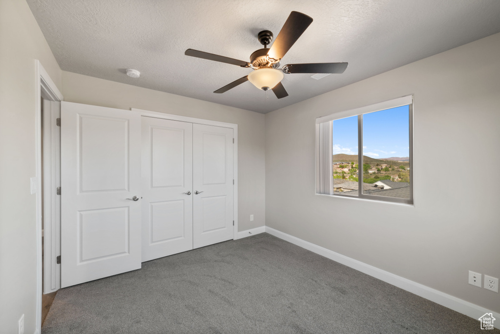 Unfurnished bedroom featuring a closet, carpet, a textured ceiling, and ceiling fan