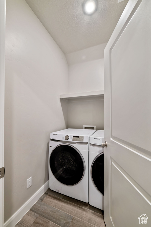 Washroom with washing machine and dryer, a textured ceiling, and hardwood / wood-style flooring