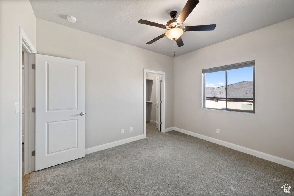 Unfurnished bedroom with ceiling fan, light carpet, a closet, and a walk in closet