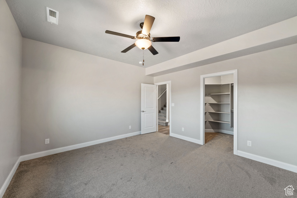 Unfurnished bedroom with light carpet, a closet, ceiling fan, and a walk in closet