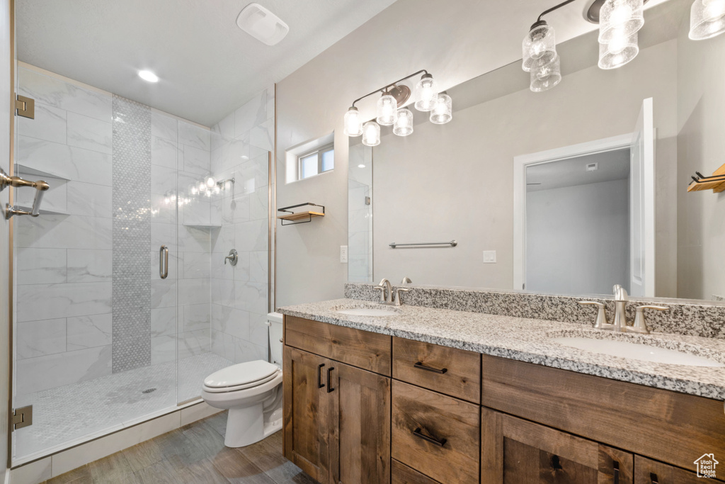 Bathroom featuring dual vanity, toilet, a shower with shower door, and wood-type flooring