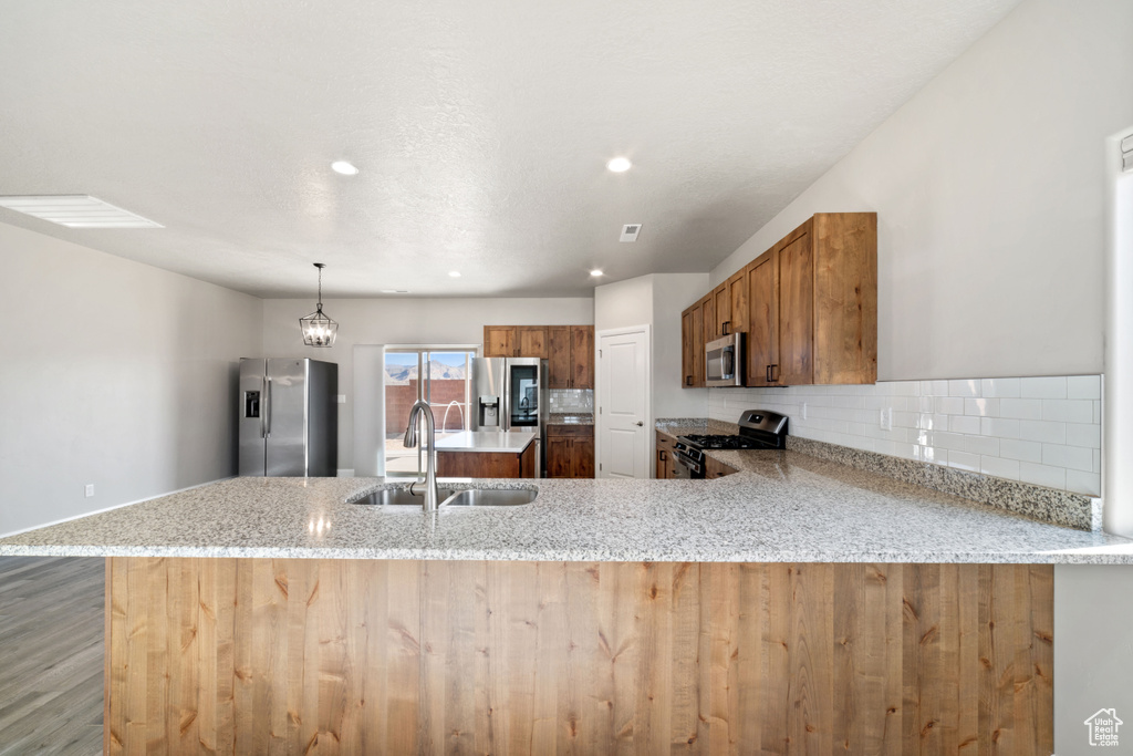 Kitchen with hanging light fixtures, hardwood / wood-style floors, sink, appliances with stainless steel finishes, and kitchen peninsula