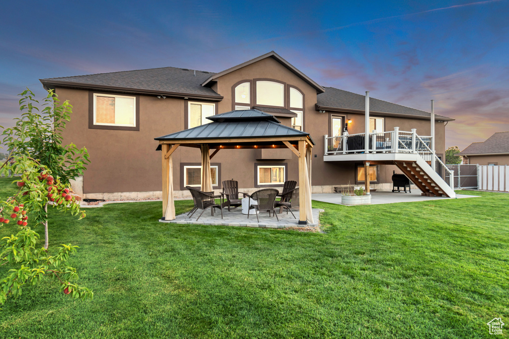 Back house at dusk featuring a deck, a lawn, a patio area, and a gazebo