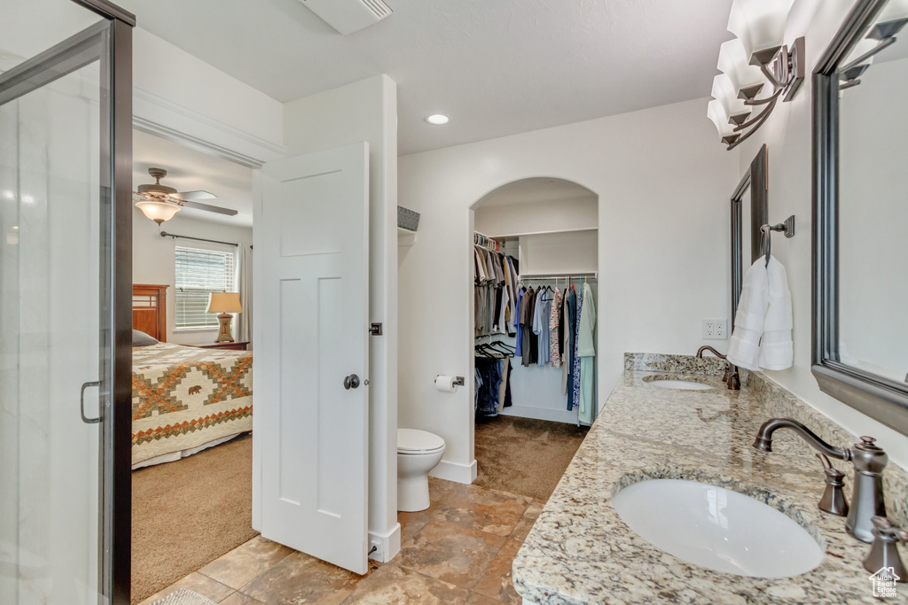 Bathroom with tile patterned floors, double sink vanity, toilet, and ceiling fan