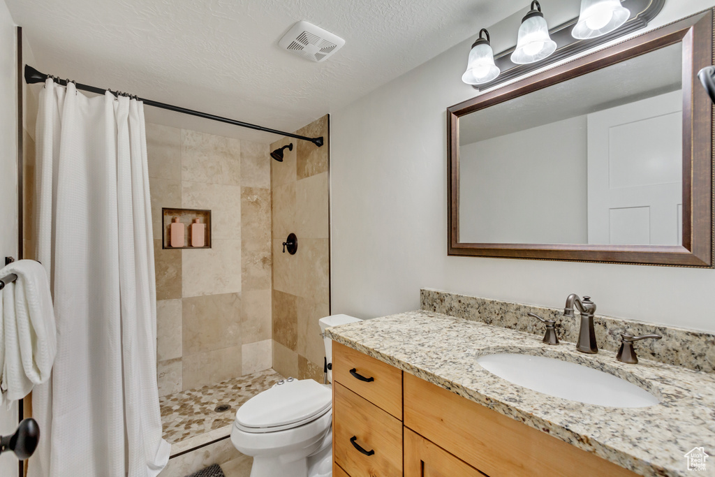 Bathroom featuring a textured ceiling, toilet, vanity, and a shower with shower curtain