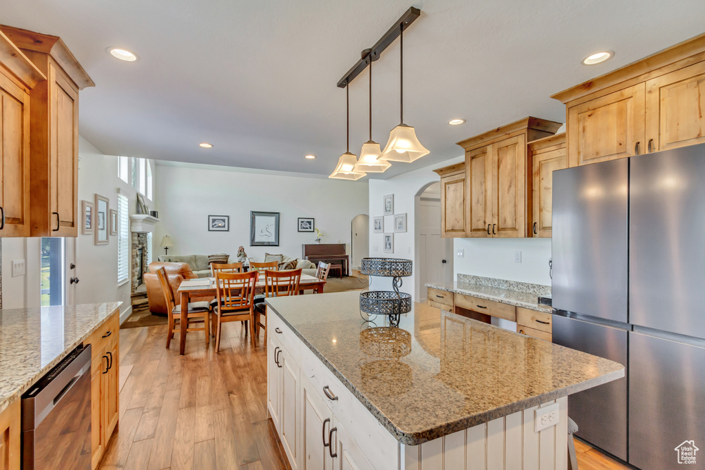 Kitchen with light wood-type flooring, light brown cabinets, light stone countertops, a kitchen island, and appliances with stainless steel finishes