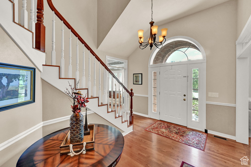 Entrance foyer with wood-type flooring, a towering ceiling, and a chandelier