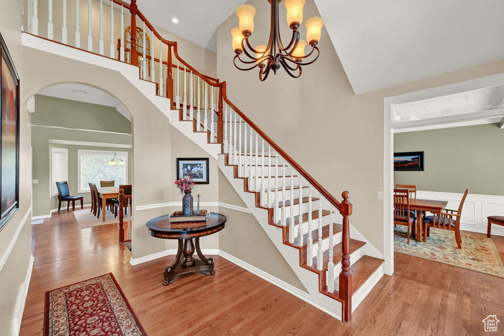 Stairs featuring a towering ceiling, a notable chandelier, and hardwood / wood-style floors