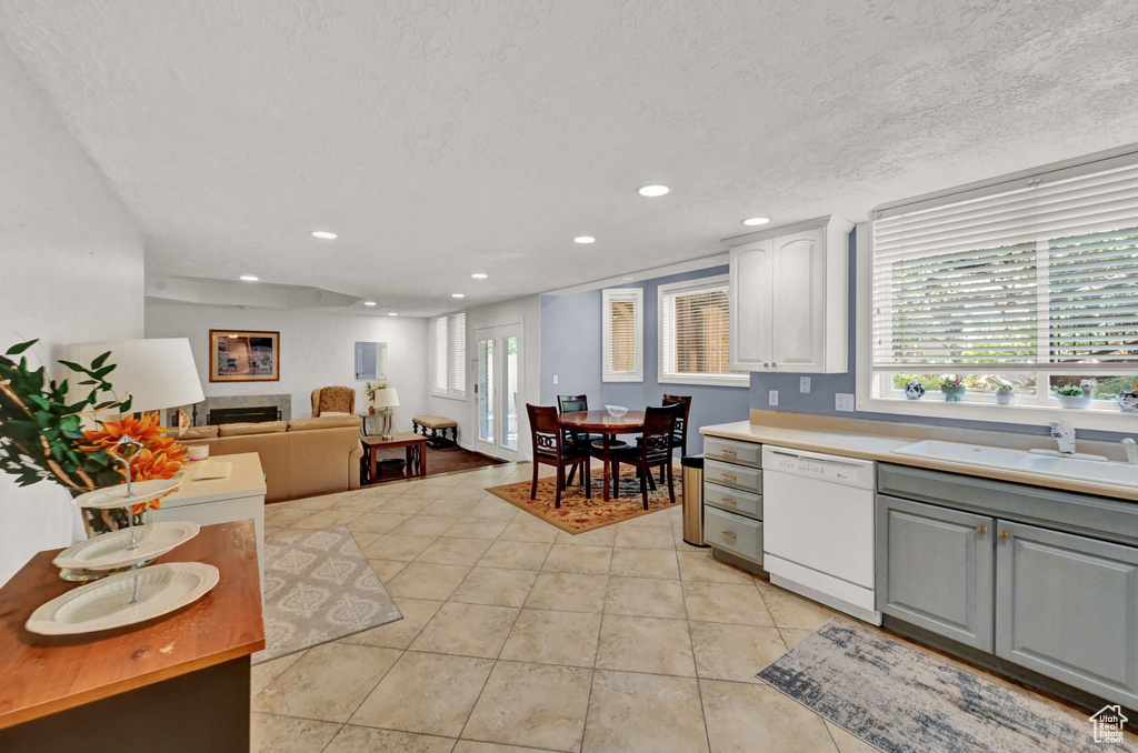 Kitchen with white dishwasher, sink, light tile patterned floors, a textured ceiling, and white cabinetry