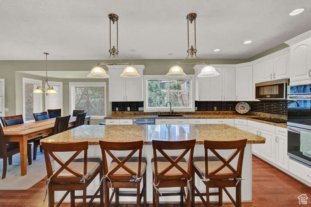 Kitchen featuring white cabinetry, hardwood / wood-style flooring, decorative backsplash, light stone counters, and a kitchen island