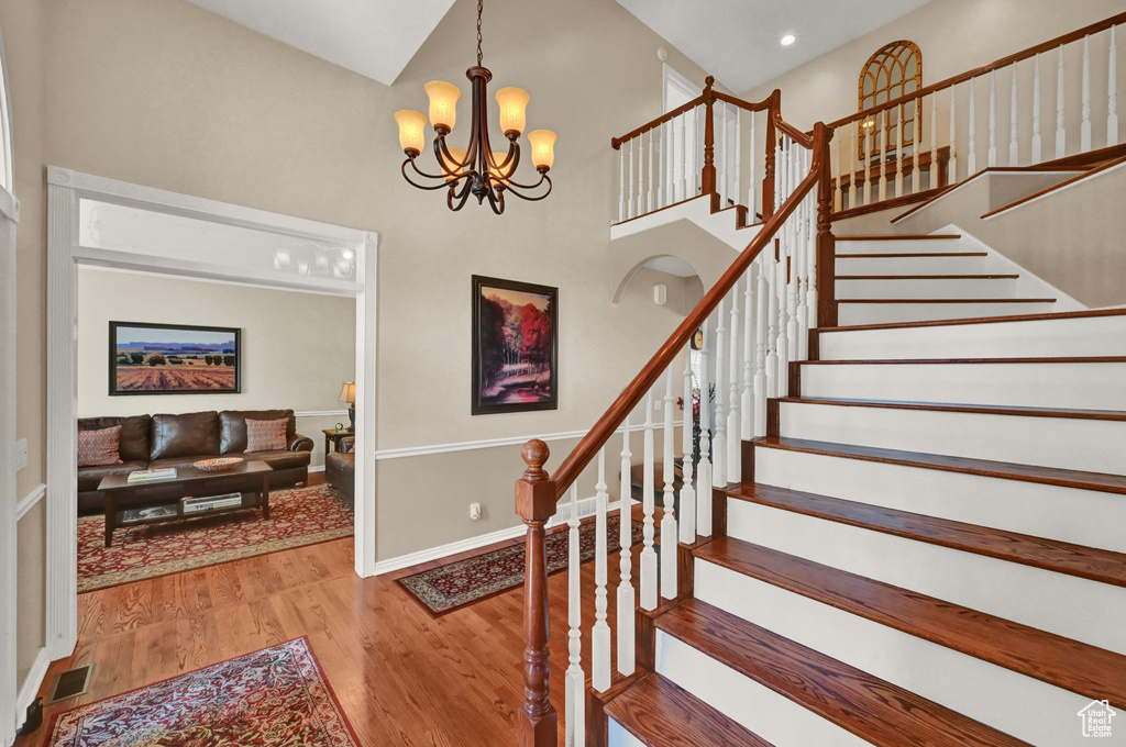 Staircase featuring high vaulted ceiling, light wood-type flooring, and a notable chandelier