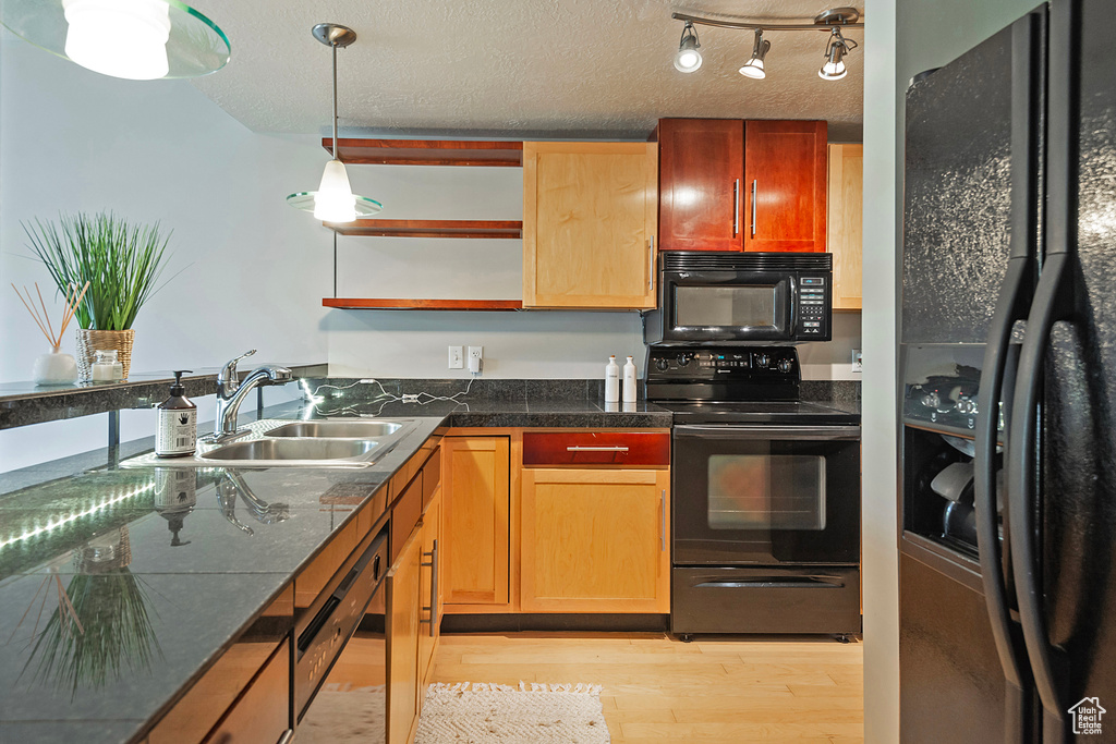 Kitchen featuring black appliances, hanging light fixtures, sink, light hardwood / wood-style flooring, and track lighting