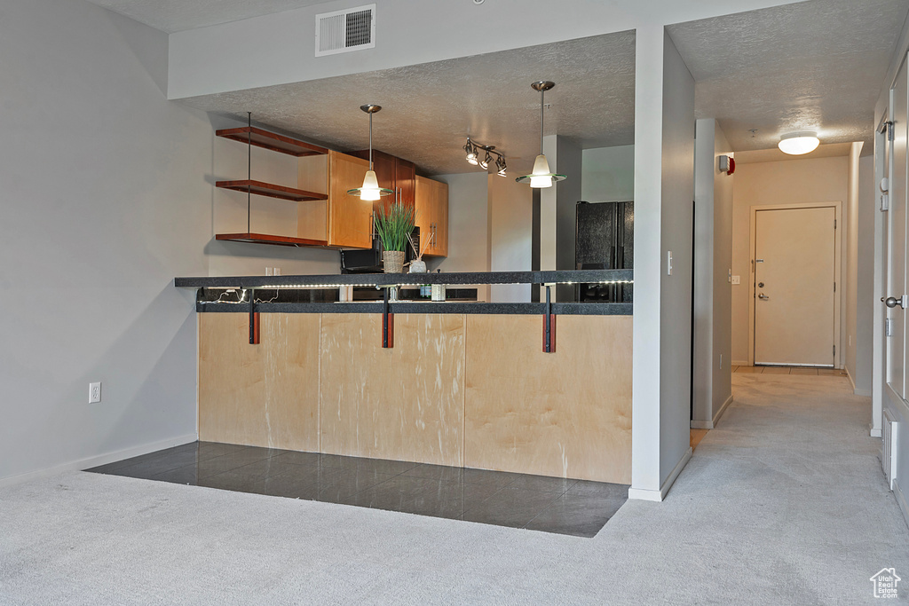 Kitchen with a textured ceiling, hanging light fixtures, kitchen peninsula, and light colored carpet