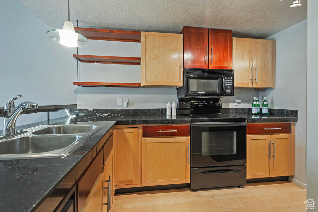 Kitchen featuring black appliances, sink, light hardwood / wood-style floors, decorative light fixtures, and a textured ceiling