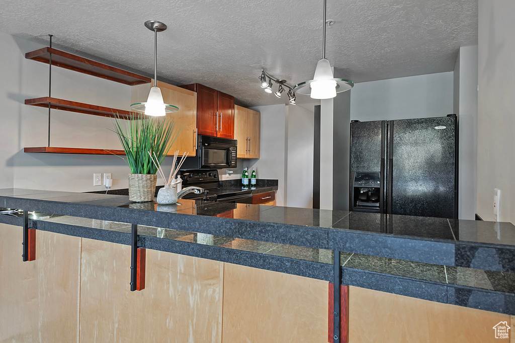 Kitchen with rail lighting, a textured ceiling, black appliances, and decorative light fixtures