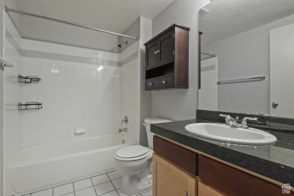 Full bathroom featuring a textured ceiling, tile patterned floors, toilet, vanity, and tiled shower / bath combo